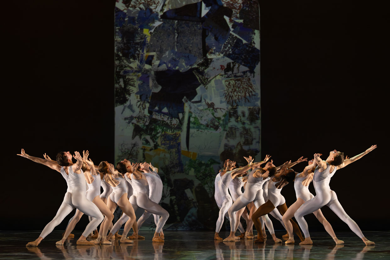 A group of dancers moving in two opposing formations on a dark stage, evoking the political choreography between left and right.
